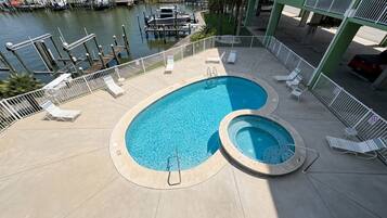 A swimming pool with lounge chairs and a hot tub, surrounded by a deck and a marina view.