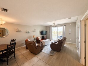 A living room with a dining table, two sofas, a TV, and a balcony with a view.