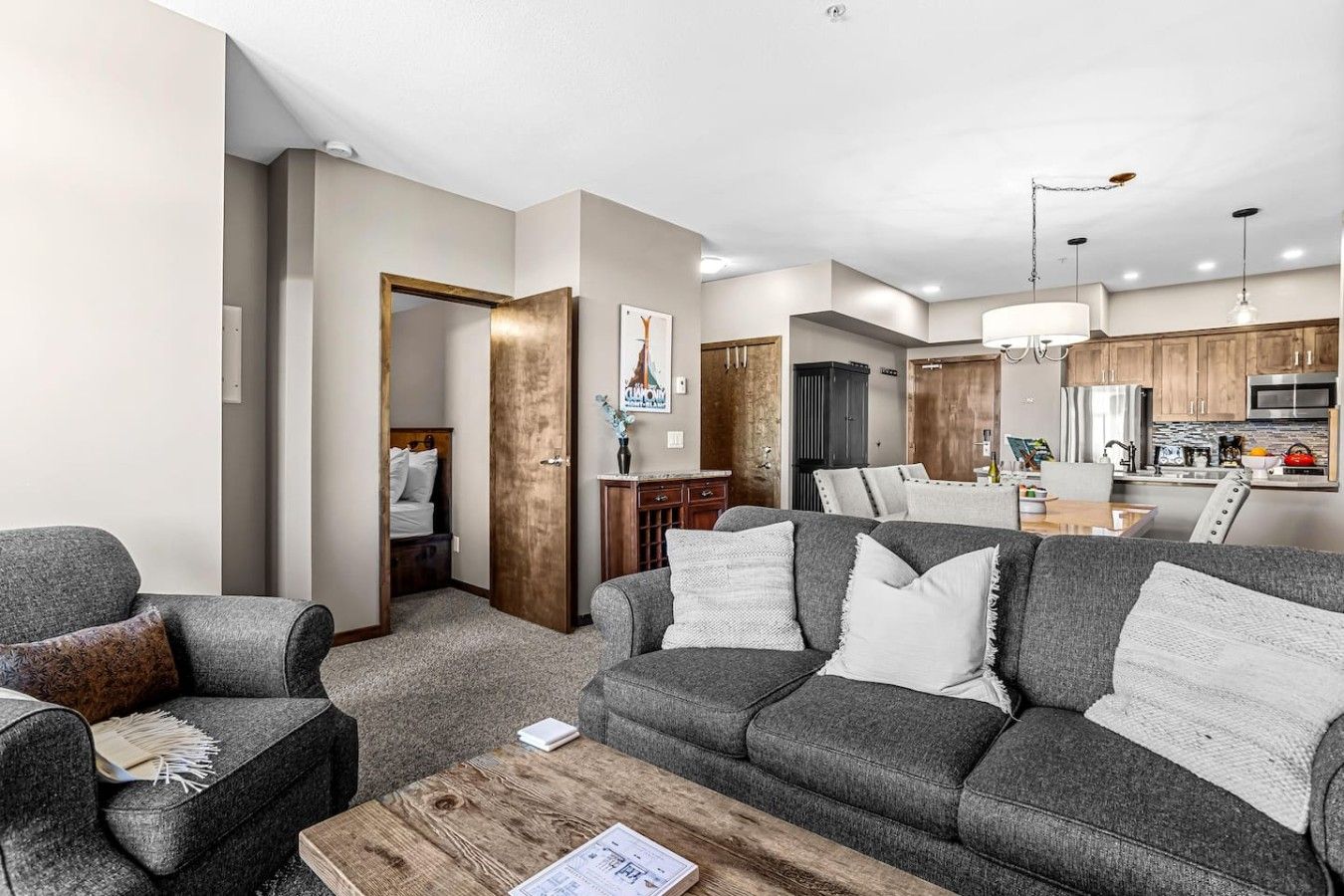 A modern living room with a grey sofa set, a wooden coffee table, and a dining area with a wooden table and chairs.