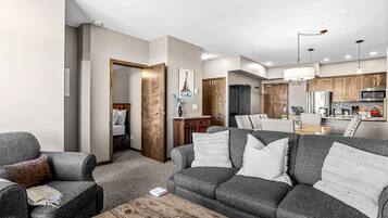 A modern living room with a grey sofa set, a wooden coffee table, and a dining area with a wooden table and chairs.