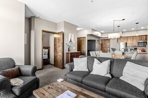 A modern living room with a grey sofa set, a wooden coffee table, and a dining area with a wooden table and chairs. - Luxe Ski-in/out Getaway Sleeps 6 Gym + Hot Tub (Golden)