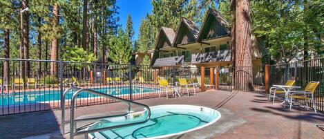 A pool area with a hot tub, lounge chairs, and a building with a sloped roof.