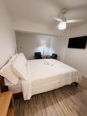 A hotel room with a bed, a desk, a chair, a floor lamp, and a ceiling fan.