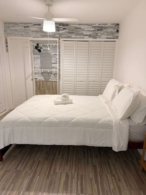 Ein Schlafzimmer mit einem Bett, einer Hängeleuchte, einem Kleiderschrank mit Schiebetüren und einem Fenster mit einem gemusterten Vorhang.