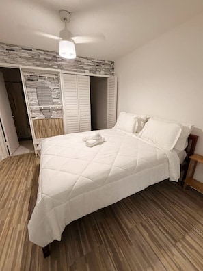 Ein Schlafzimmer mit einem Bett, einem Deckenventilator, einem Kleiderschrank und Holzboden.