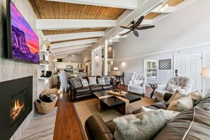 Ein geräumiges Wohnzimmer mit Kamin, Ledersofas, einem Couchtisch und einem Deckenventilator.