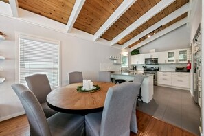 Une cuisine moderne avec des meubles blancs, un îlot central et un coin repas comprenant une table ronde et des chaises.