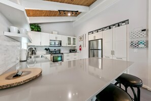 Une cuisine moderne dotée d’un grand îlot central, d’appareils électroménagers en acier inoxydable et de meubles blancs.