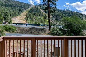 A mountain view with a road, a building with a green roof, and a wooden deck in the foreground. - 3829S Heavenly View Across from Heavenly Cal Base Lodge (South Lake Tahoe)