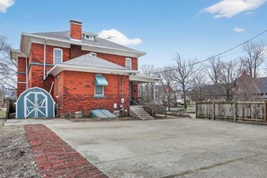 Une maison à deux étages, construite en briques, avec un porche à l’avant et une porte de garage.