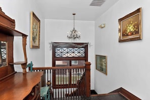A staircase with a wooden railing, a chandelier, and framed artwork on the walls.