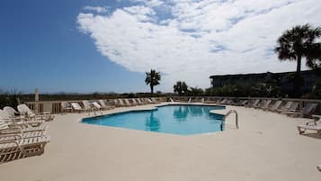 A pool area with lounge chairs, a palm tree, and a building in the background.