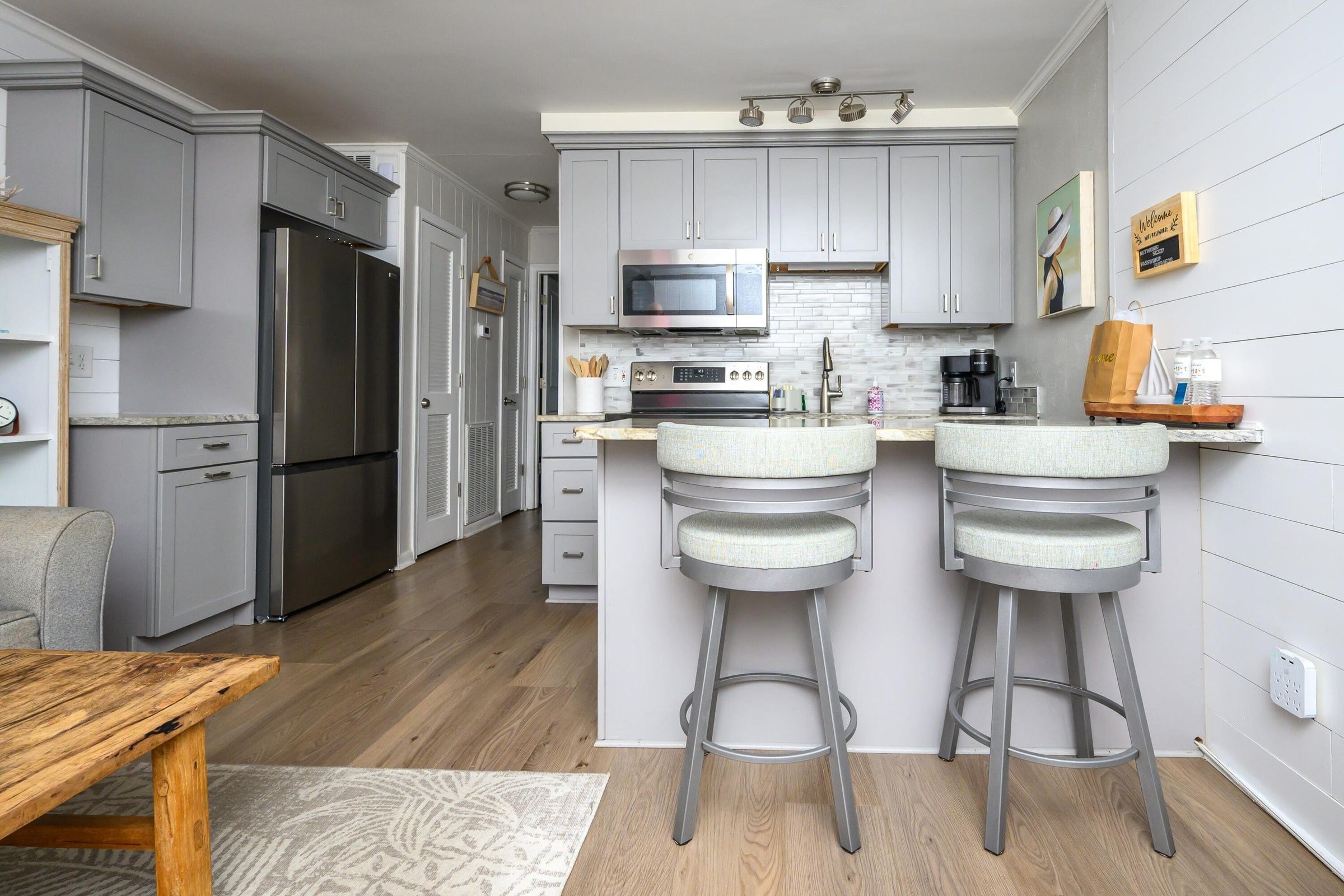 A modern kitchen with grey cabinetry, stainless steel appliances, and a bar area with stools.