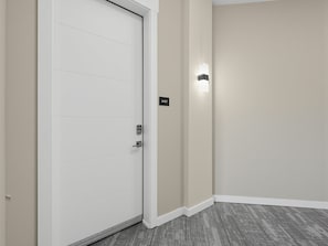 A hallway with a white door, a wall-mounted light, and a carpeted floor. - Brand-New Luxury Furnished Penthouse in NoDa, MidTerm Rental (Charlotte)