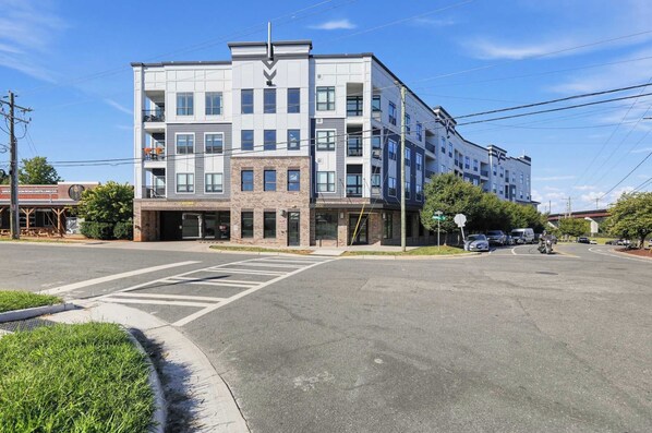 A multi-story building with a commercial ground floor, a parking lot, and a clear sky.