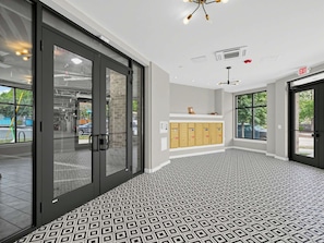 Un intérieur moderne avec un sol à motifs géométriques, une porte d’entrée en verre et une vue sur l’extérieur.