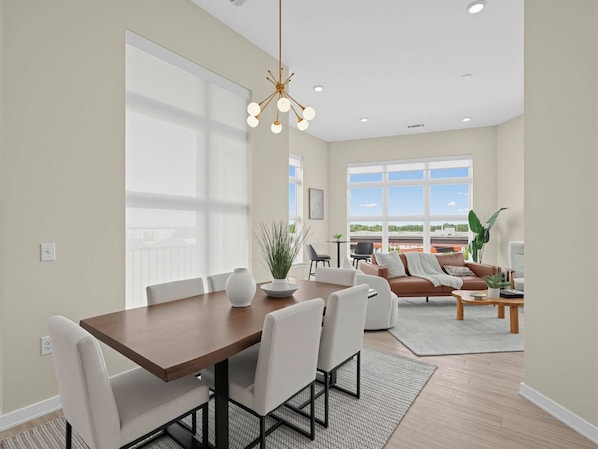 A modern interior with a dining area, a living room, and large windows. - Brand-New Luxury Furnished Penthouse in NoDa, MidTerm Rental (Charlotte)