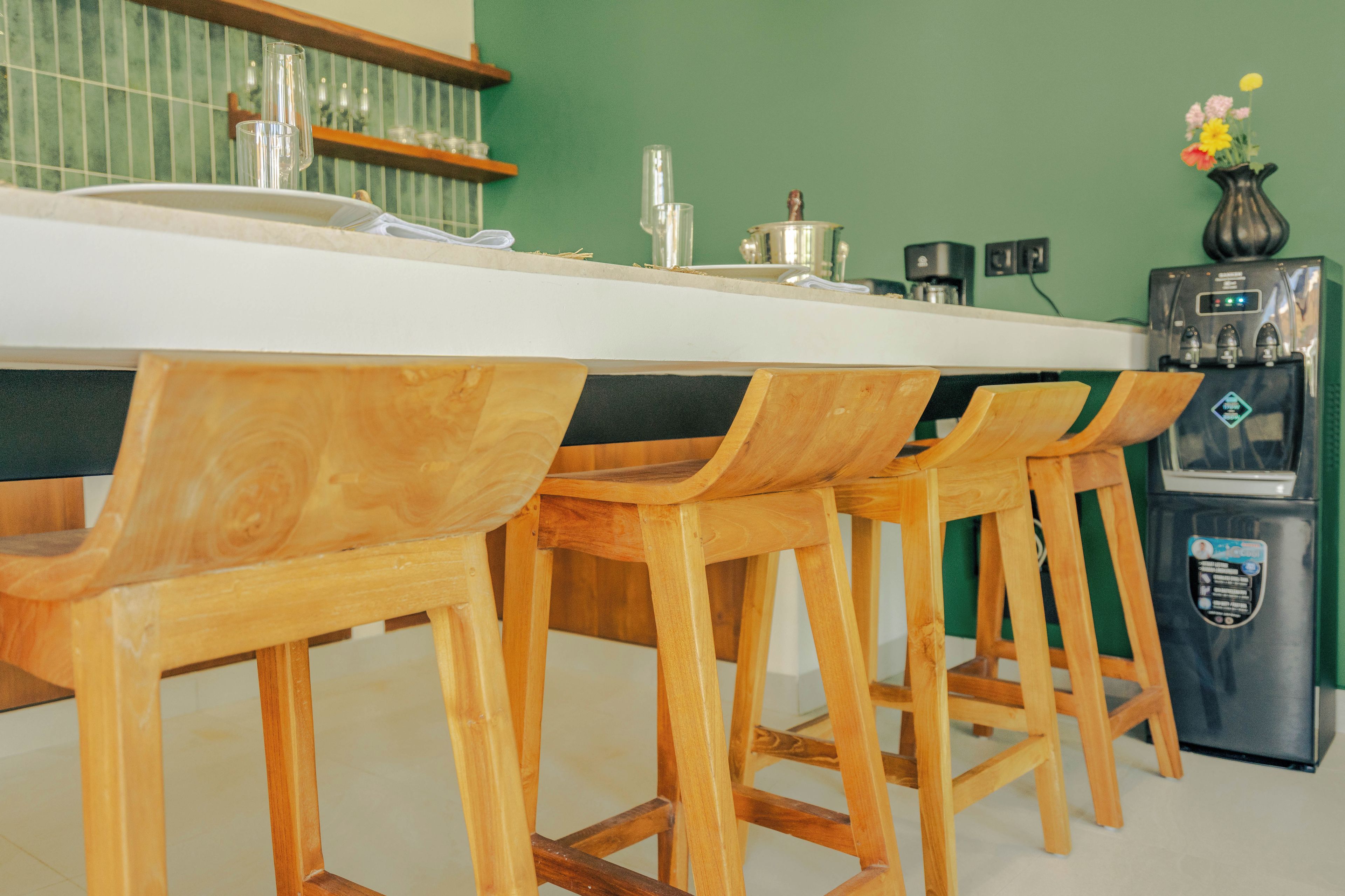 Une cuisine avec un plan de travail blanc, des tabourets de bar en bois, une machine à café et un réfrigérateur.