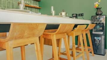 Une cuisine avec un plan de travail blanc, des tabourets de bar en bois, une machine à café et un réfrigérateur.
