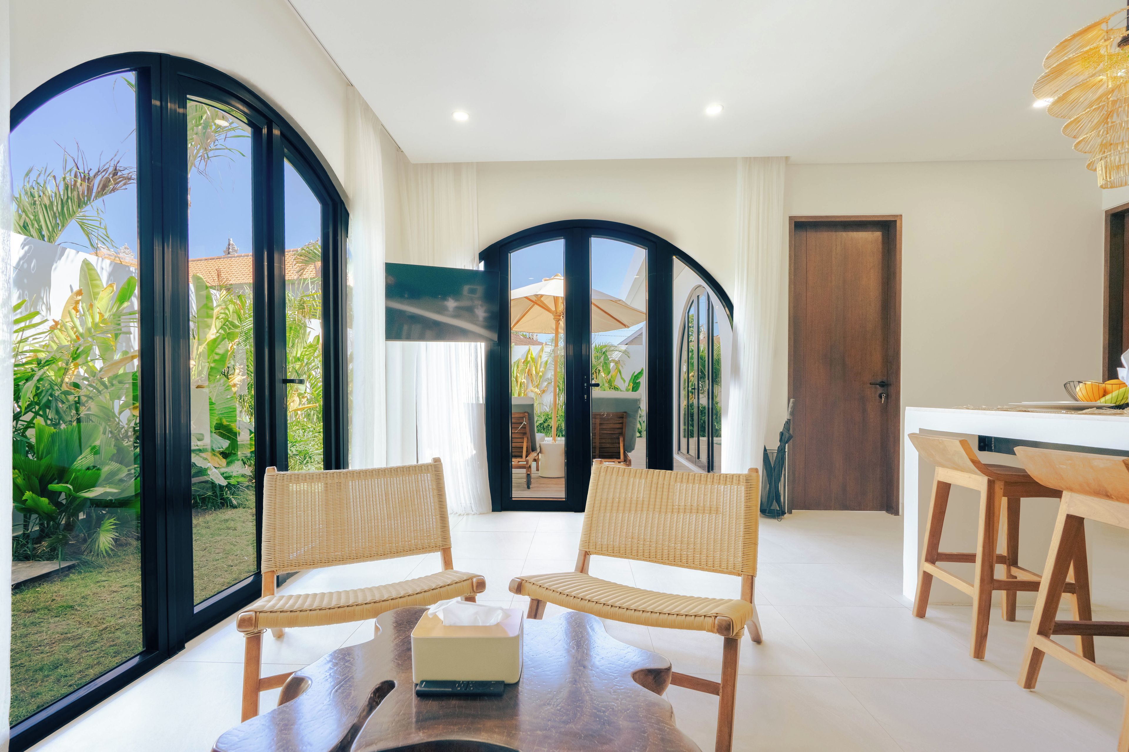 A modern living room with large windows, a dining area, and a view of a garden.