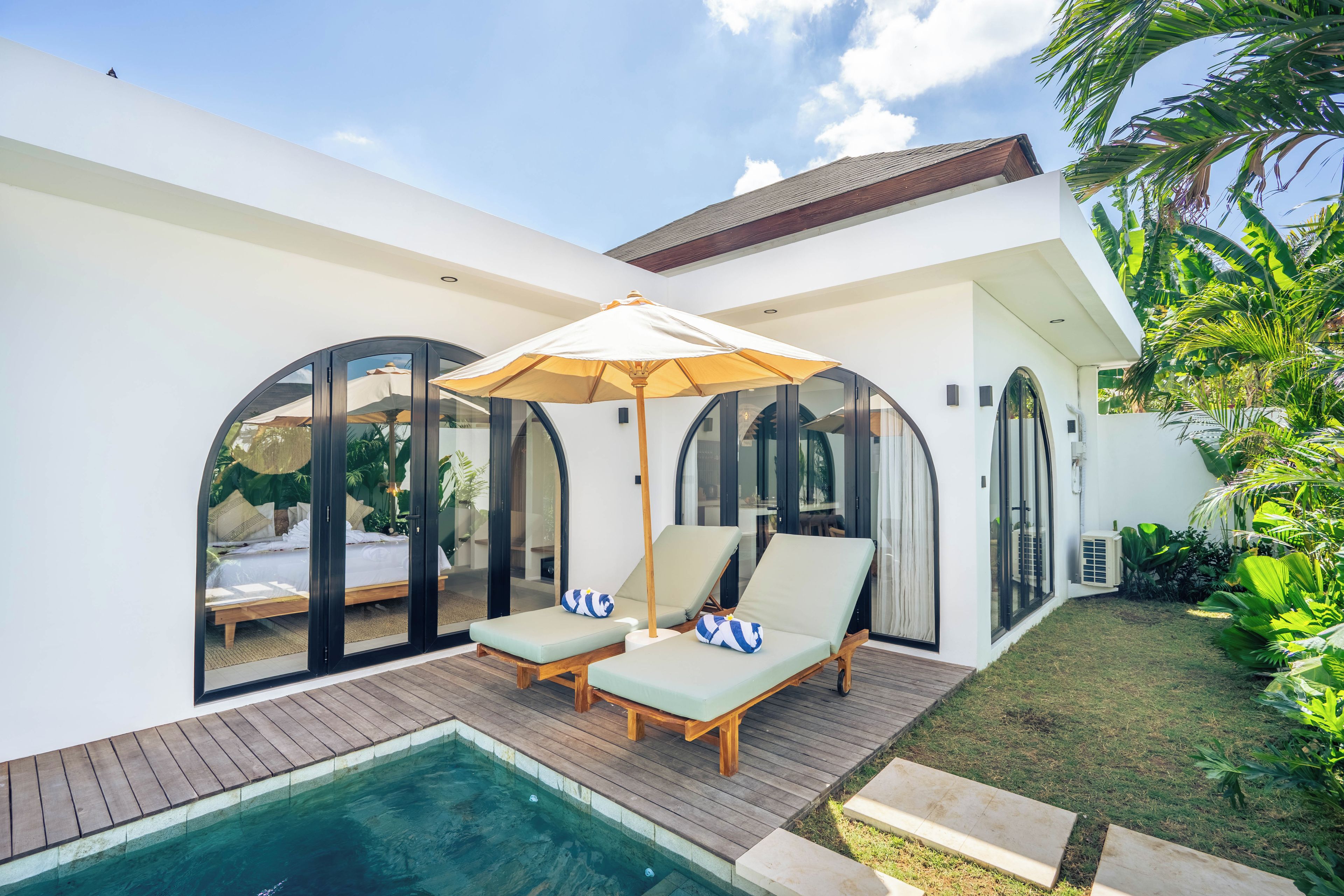 Uma casa moderna com piscina, duas espreguiçadeiras e um grande guarda-sol.