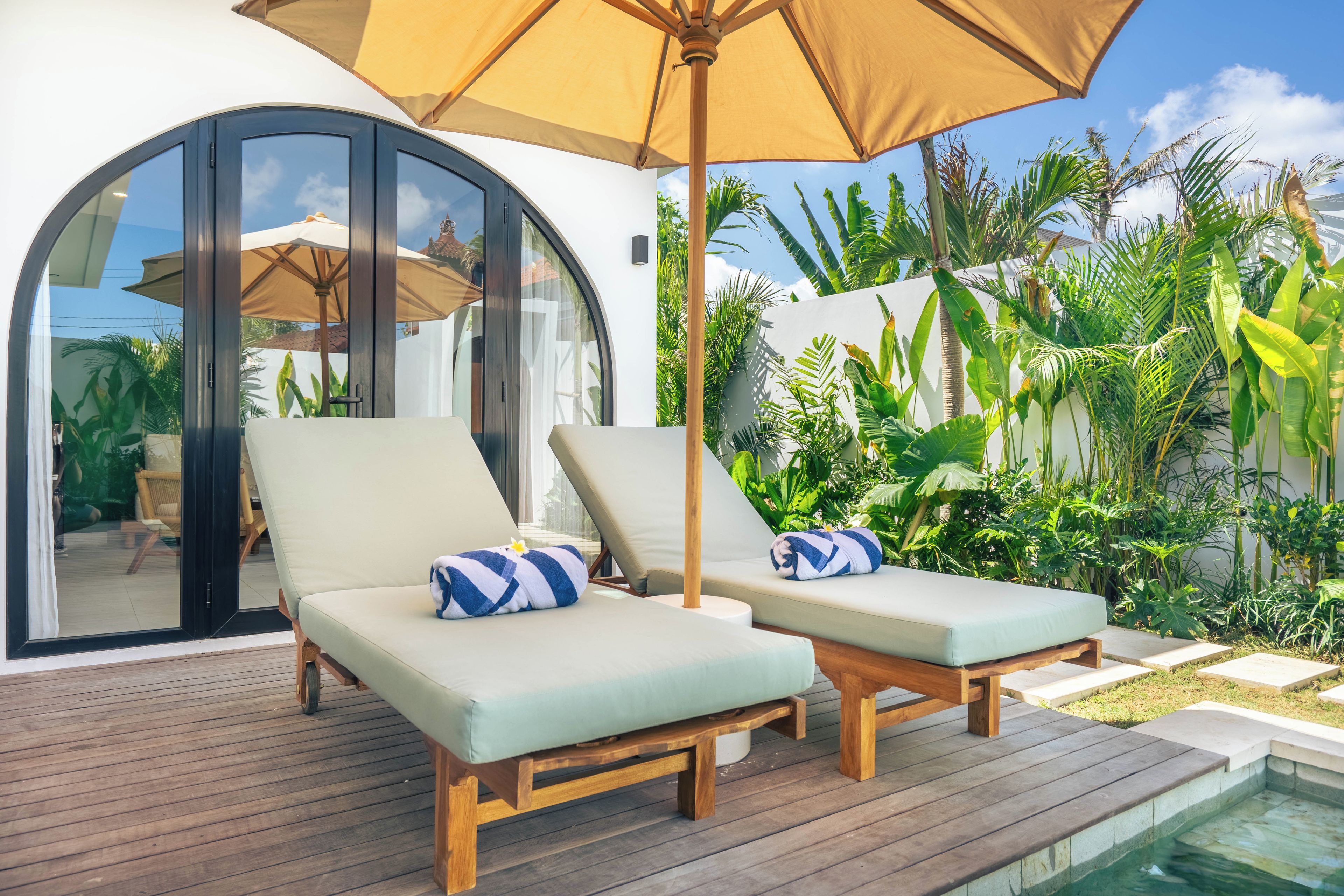 A deck with two lounge chairs, a wooden pool, and lush tropical plants.