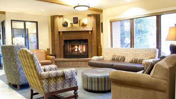 Una sala de estar acogedora con chimenea, asientos cómodos y un amplio ventanal con persianas.