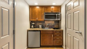 Una cocina compacta con armarios de madera, un microondas de acero inoxidable, una cafetera y un lavavajillas.