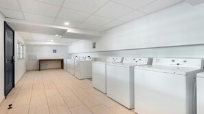 Een wasserette met meerdere witte wasmachines en drogers, een houten bankje en een betegelde vloer.