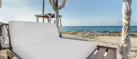A beachside bed with a view of the ocean, a wooden structure, and a beach in the background.