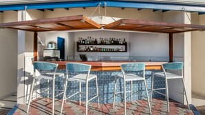 Ein Außenbereich mit Bar, der einen Holz-Pergola, eine Theke und vier Barhocker mit gemusterten Kissen bietet.