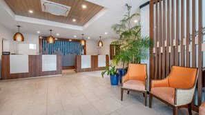 Ein Hotel-Empfangsbereich mit einem Holzbüro, zwei Angestellten und einer großen Topfpflanze.
