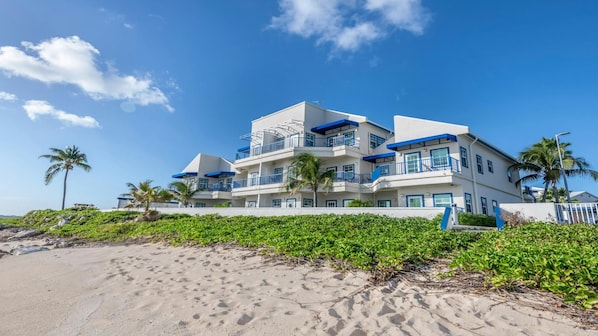 Ein mehrstöckiges Strandhotel mit Balkonen, Palmen und einem Sandstrand im Vordergrund.