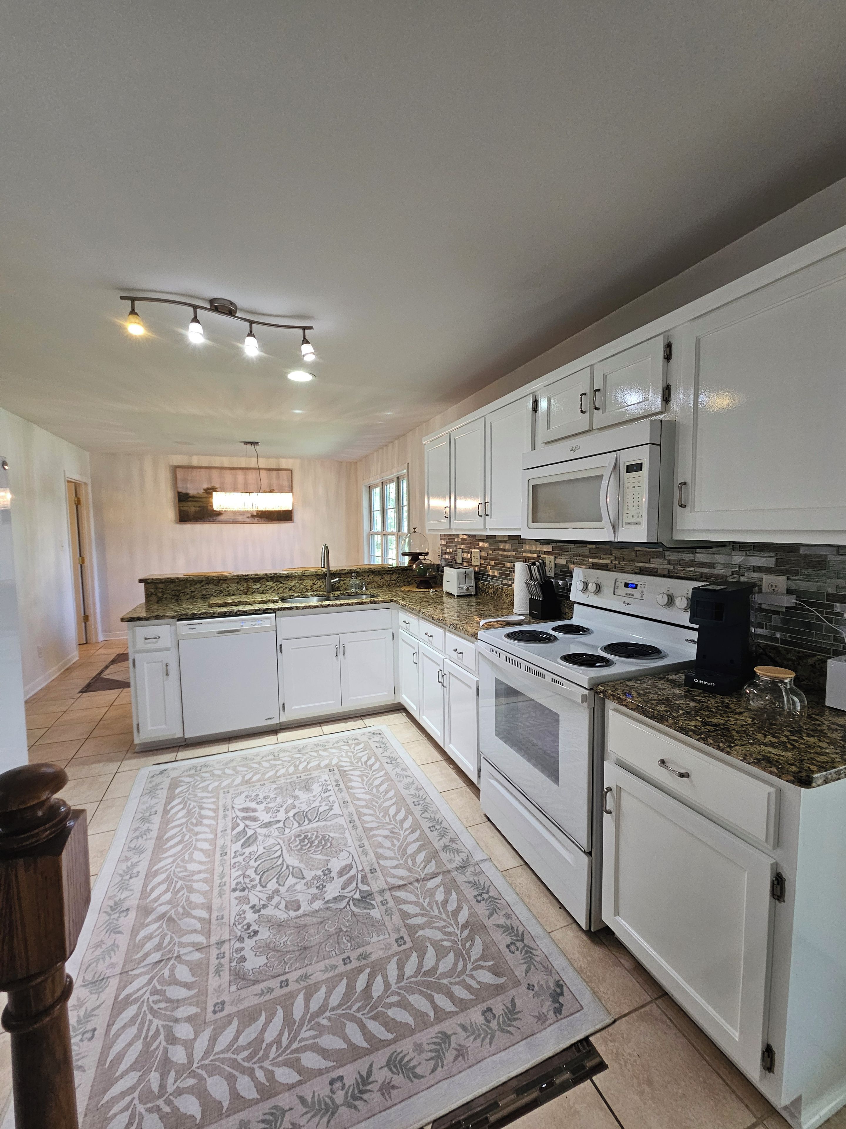 A modern kitchen with white cabinetry, a granite countertop, a built-in microwave, a stove, and a coffee maker.