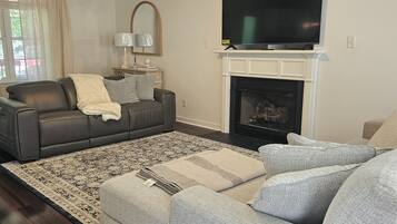 Un salon avec une cheminée, un téléviseur, un ventilateur de plafond et un grand tapis.