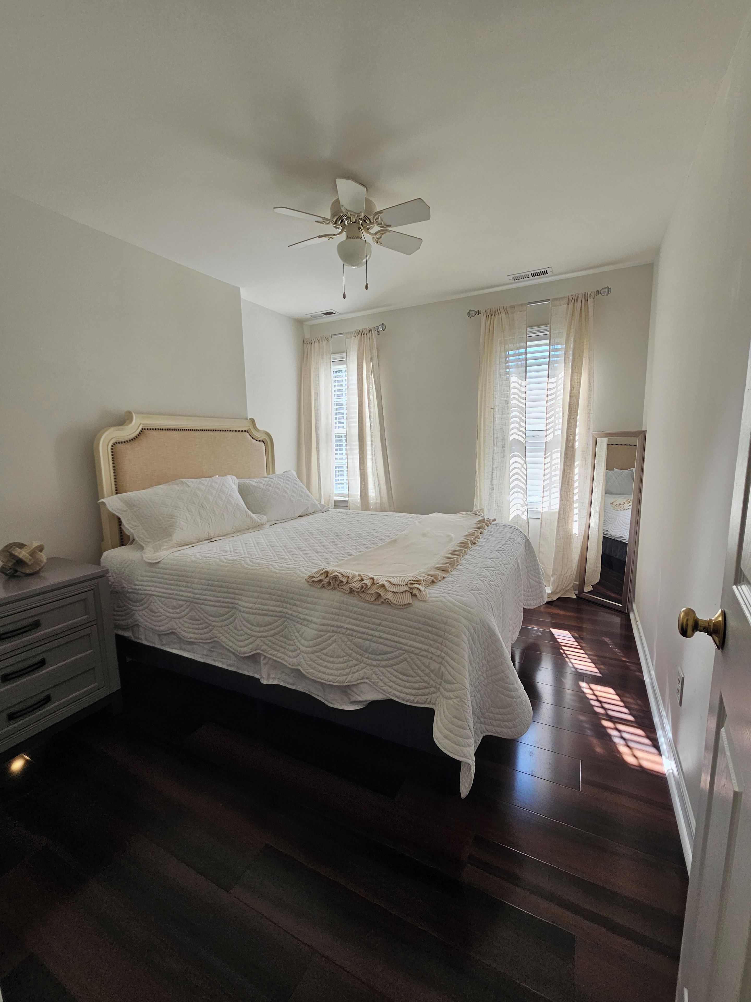Une chambre à coucher comprenant un lit, une table de chevet, un ventilateur de plafond et une porte dotée d’une poignée en laiton.