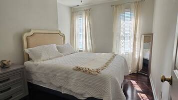 Une chambre à coucher comprenant un lit, une table de chevet, un ventilateur de plafond et une porte dotée d’une poignée en laiton.