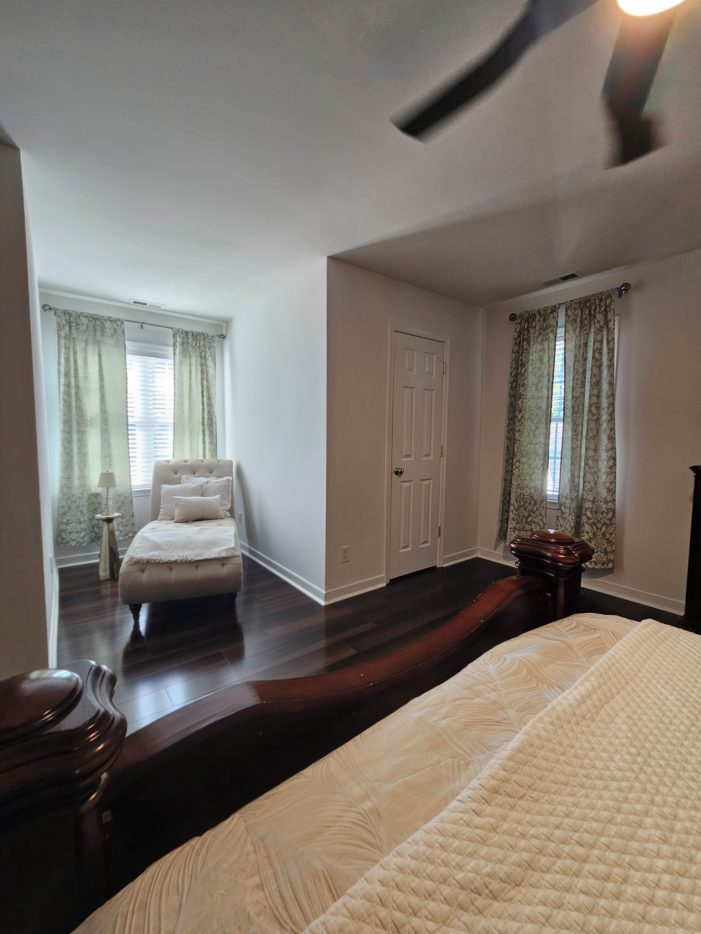 Une chambre à coucher avec un grand lit, une commode, une table de chevet, un ventilateur de plafond et une porte.