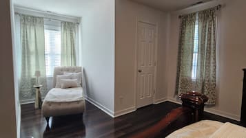 Une chambre à coucher avec un grand lit, une commode, une table de chevet, un ventilateur de plafond et une porte.