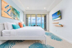 Une chambre d’hôtel moderne avec un grand lit, une vue sur l’océan et des œuvres d’art accrochées aux murs.
