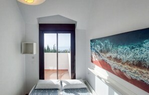 A room with a bed, a door leading to a balcony, and a large painting of ocean waves. - Apartamento Benalmadena vistas (Benalmadena)