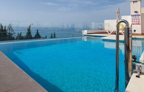 A clear blue pool with a glass barrier, a lifeguard stand, and a view of the sea. - Apartamento Benalmadena vistas (Benalmadena)