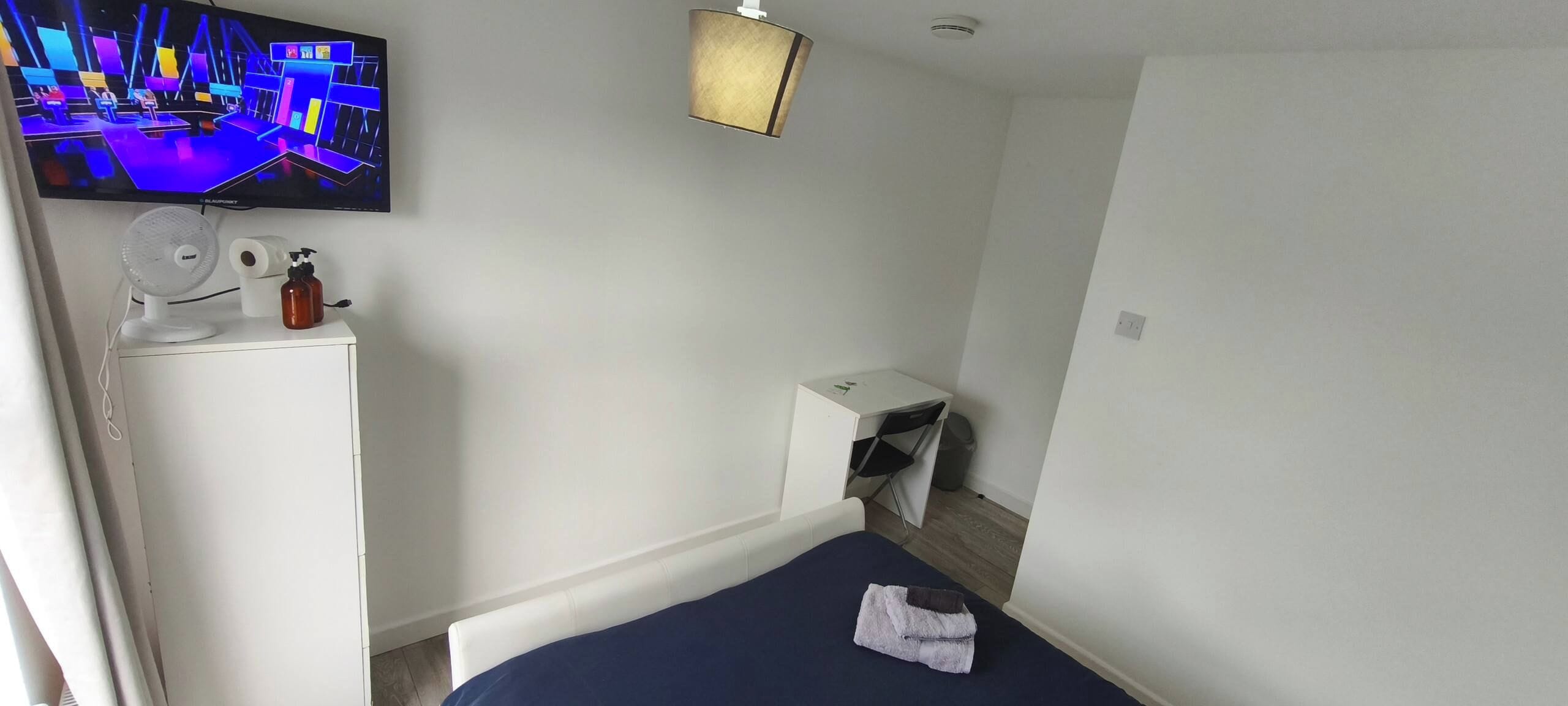 Habitació d'hotel petita amb un llit, escriptori, cadira, televisor i paperera.