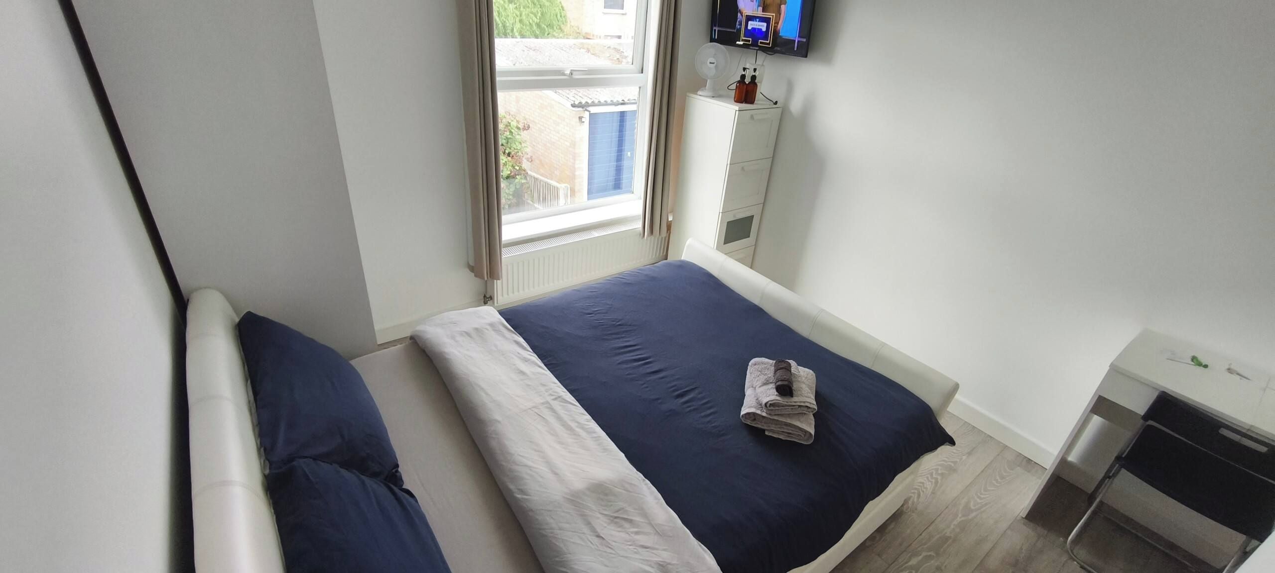 Una camera da letto con un letto, una finestra, una TV e un piccolo mobiletto.