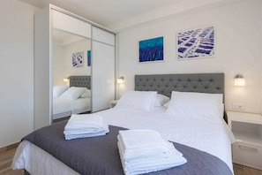 Une chambre d’hôtel avec un grand lit, un miroir, deux tableaux accrochés au mur et une table de chevet avec une lampe.