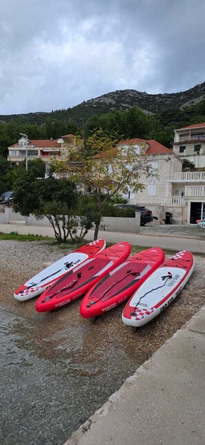 Une rangée de planches de surf rouges et blanches sur une surface de galets, avec un bâtiment et des arbres en arrière-plan.