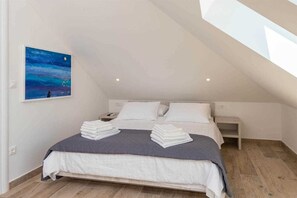 A modern bedroom with a sloped ceiling, a bed with white linens, a nightstand, and a painting of a night sky. - Villa Oaza Ora | Private pool & Beach nearby, Pelješac (Kučište)