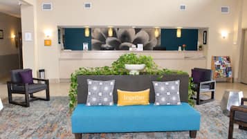 Un vestíbulo con una recepción, un sofá azul con cojines estampados y dos sillones.