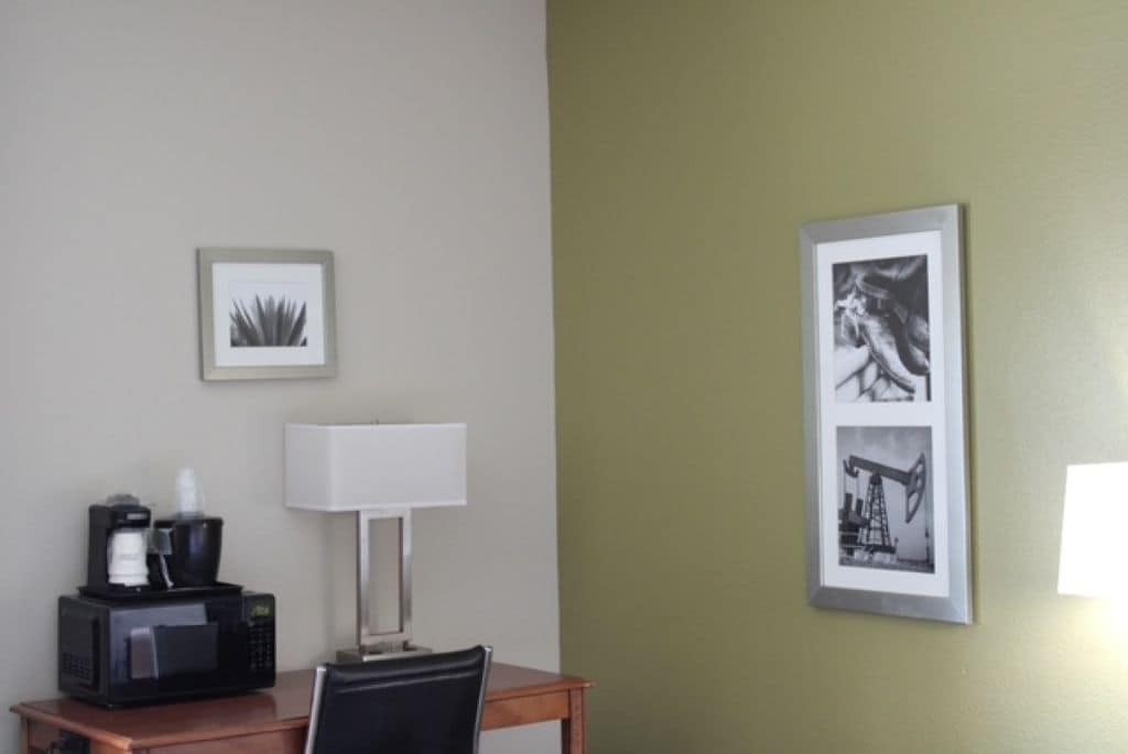 A hotel room with a desk, a lamp, a framed picture, and a coffee maker.