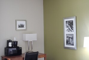 Una habitación de hotel con escritorio, lámpara, un cuadro enmarcado y cafetera.